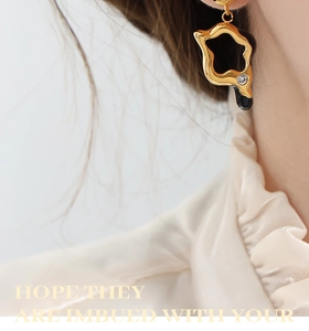 Detail of gold geometric hollow star earrings with black enamel and clear zircon stones