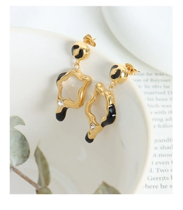 Irregular gold geometric earring with black enamel and diamond accent on a white bowl