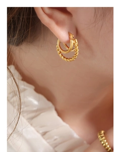 Détail de boucles d'oreilles en U dorées torsadées portées sur un fond de tissu blanc texturé