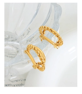 Détail de boucles d'oreilles doubles dorées avec texture torsadée sur du verre