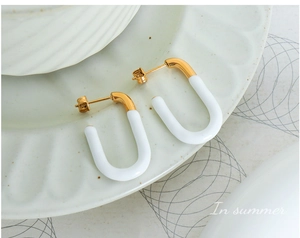 Macro detail of U-shaped gold earrings with white enamel finish on a white ceramic plate