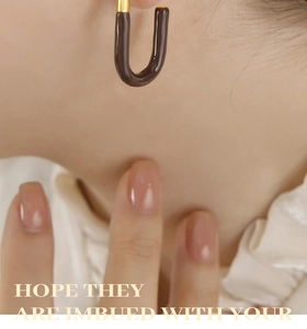 Detailed macro view of U-shaped gold earrings with dark brown enamel finish on model