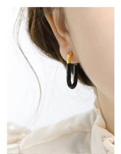 Close-up of minimalist G-shaped gold-plated earrings with black drip oil enamel finish