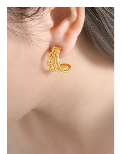 Close-up of gold-plated twisted earrings with hollow design worn on a person ear