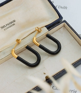 Detail of G-shaped gold-plated earrings with black resin inlay on a vintage blue gift box