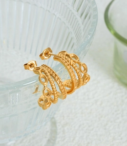 Detailed close-up of triple-layered twisted gold-plated titanium earrings on glass