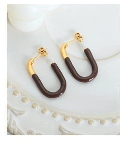 Detail view of geometric G-shaped gold plated earrings with brown enamel oil on porcelain