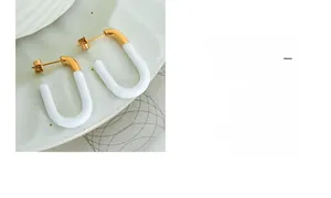 Detail view of U-shaped gold-plated metal and white enamel earrings on a ceramic dish