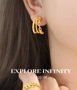 Close-up of gold-plated twisted woven earrings and link ring on a female model