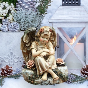 Detailed close-up of a resin angel statue with flower wreath and wings in snowy scenery