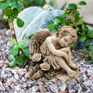Garden angel figurine sitting with wings and roses in a peaceful outdoor plant setting