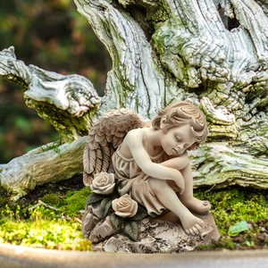 Detail of sleeping angel garden ornament with white roses on mossy forest ground