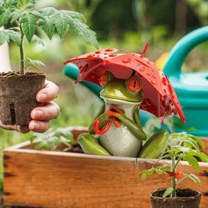 Detailed garden stake of a green tree frog under a red umbrella with realistic water drops