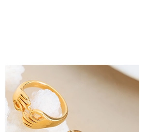 Detailed macro view of gold hug rings on white coral against a minimalist beige background