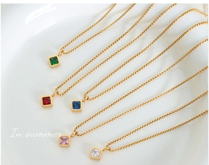Detail of colorful square gemstone pendants on gold box chains atop a ceramic tray