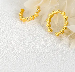 Macro shot of gold ear cuffs with embossed heart patterns on a white textured backdrop