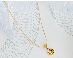 Close-up of a gold-plated Xi symbol pendant necklace on a frosted glass textured surface