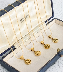 Detail view of four gold-plated necklaces with hollow Fu character pendants in a luxury box