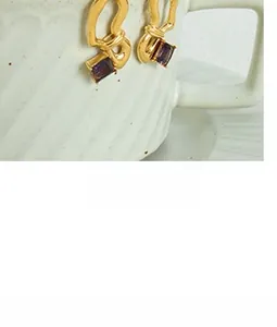 Macro shot of gold geometric earrings with square purple stones on white ceramic cup