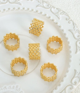 Detail of six gold honeycomb mesh rings with cubic zirconia on a white vintage plate