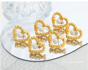 Close-up of heart-shaped gold earrings with central pearl and beaded texture finish
