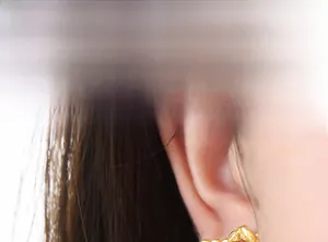 Detailed close-up of a gold-plated textured hoop earring worn on a model's ear