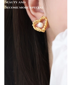 Close-up of gold heart-shaped earring with pearl inlay worn by a model