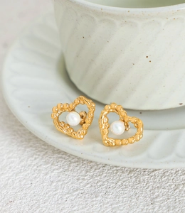 Detail view of gold heart earrings with braided texture and white pearl inlay