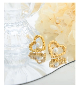 Detail of heart-shaped gold studs with center pearl on a reflective mirror surface