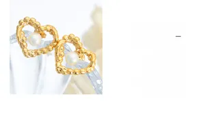Close-up of heart-shaped gold earrings with textured frames and central pearl inlay