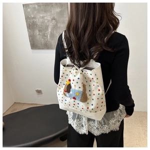 Close-up of white canvas drawstring backpack with colorful polka dots and 3D plush puppy
