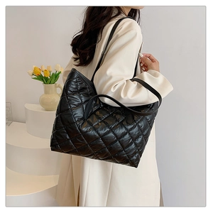 Détail d'un grand sac cabas noir matelassé avec fini brillant porté par un mannequin en studio