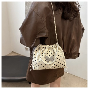 Close-up of bucket bag with black polka dots, pearl handle and metal butterfly detail