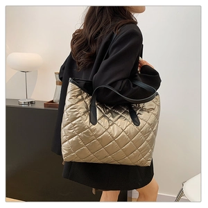 Détail du grand sac cabas matelassé doré avec anses noires porté à l'épaule