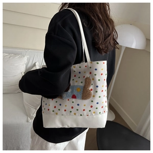 Close-up of a white tote bag featuring colorful dots and a brown plush teddy bear patch
