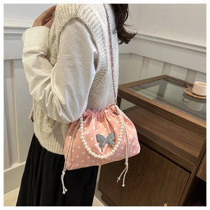 Pink polka dot drawstring bucket bag with a silver butterfly charm and pearl handle
