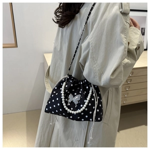 Detail of black polka dot bucket bag featuring pearl handle and silver butterfly charm