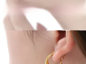Gros plan de boucles d'oreilles incurvées en titane doré avec perle sur l'oreille du mannequin