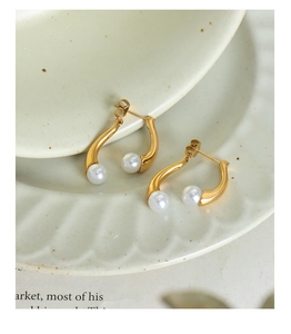 Détail des boucles d'oreilles courbées plaquées or avec perles sur un plateau en céramique