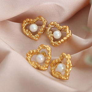 Asymmetric hollow heart stud earrings with white pearl center on silk fabric