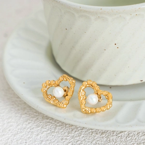 Elegant gold heart earrings with white pearls on a minimalist ceramic dish display