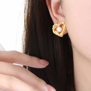 Elegant gold heart earrings with textured frame and white round pearl on female model