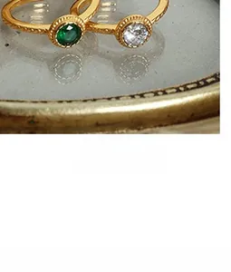 Détail de bagues vintage plaquées or avec pierres émeraude et diamant sur plateau métal