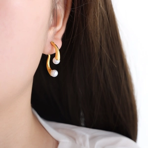 Boucles d'oreilles courbées dorées en titane avec perles présentées sur un mannequin