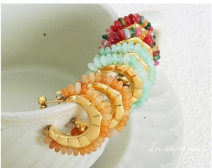 Detail of C-shaped gold plated earrings with colorful natural stone beads on a cup