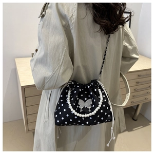 Detail of black polka dot bucket bag with pearl handle and silver butterfly buckle on model