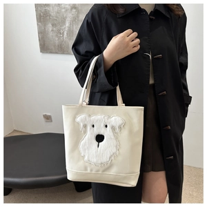 Detail of white leather tote bag featuring a cute schnauzer plush patch and sturdy handles