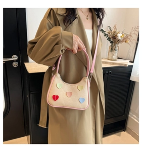 Dettaglio borsa beige intrecciata con cuori 3D colorati e tracolla in pelle rosa