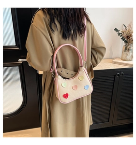 Dettaglio borsa in tela con cuori colorati e rifiniture in pelle rosa indossata dal modello