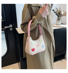 Dettaglio di una borsa beige con cuori colorati abbinata a un trench kaki e fiori d'arredo